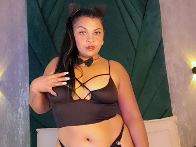 BrunetteScarlet with black cat ears, wearing a black strappy top and black panties, touching her tits, choker with bowtie, long black hair, pouty lips, standing, bedroom.