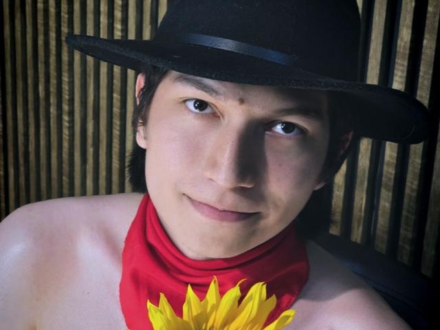 ErossGuy with a black hat, red scarf, and yellow flower in front, has a cute face, dark eyes, and a subtle smile, looking directly at the camera.