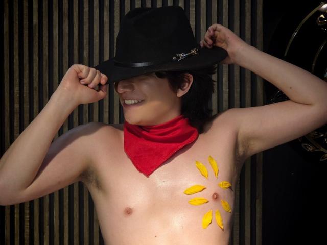 ErossGuy is shirtless, wearing a black hat and red bandana, with yellow bananas on his chest, smiling, and touching his hat. He has a slim build and light skin.