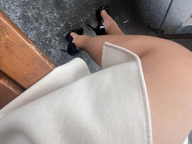 OndinaNoir's bare ass and legs in black high heels, standing on a grey textured floor, with a beige fabric covering part of her lower back.