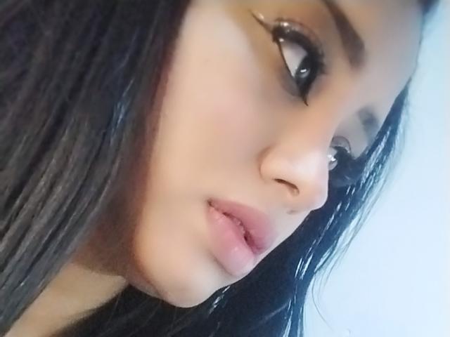 MariaCatalina's face, showing her pouty pink lips, glossy black eyes, and long wet black hair, with a slight upshot of her nose and smooth fair skin.