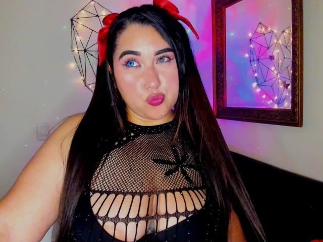 MadeleineDeveraux with long black hair, red bow, blue eyes, wearing black fishnet top with cut-out, pouty pink lips, fair skin, small to medium tits, looking at camera.