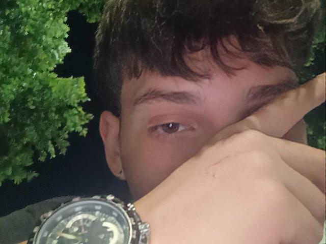JonathanMoreau's face is partially obscured by a hand, showing a wristwatch with a black and white face, brown curly hair, and a slightly confused expression in a nighttime photo.
