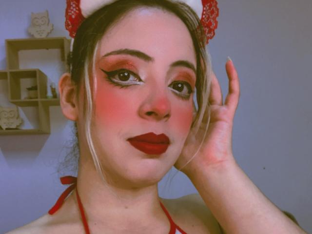 Rosalines has red lipstick, red eyeshadow, and a red bow, with her hand touching her face. She's wearing a red halter top, and has a slight blush.