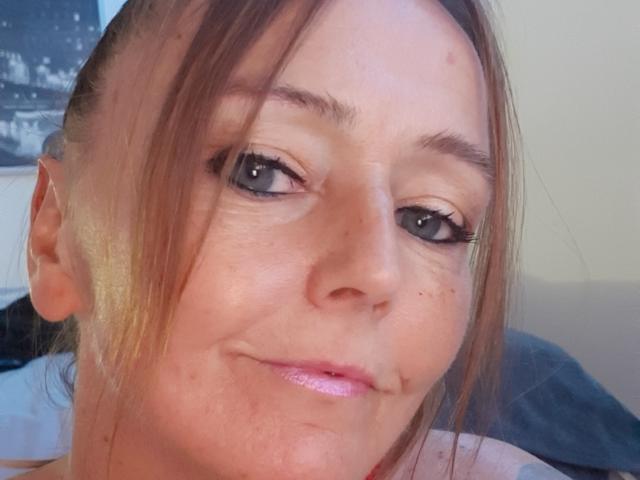 MissFreeBird has light brown hair, blue eyes, and a slight smirk with pink glossy lips. Her freckled face shows a small pimple near her right cheek.