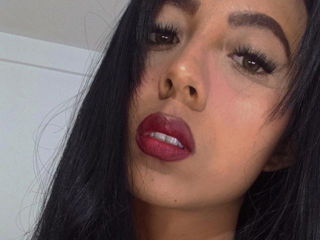 DaphneSpencer's face with dark, wavy hair, brown eyes, thick eyebrows, and full, red lips slightly parted. Her skin is light brown, and she has long, dark eyelashes.