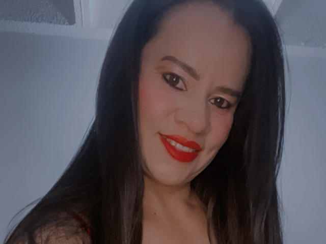 CharllotI has long black hair, red lipstick, and a slight smile with red eyes, wearing a black lace top. Her ass is not visible.