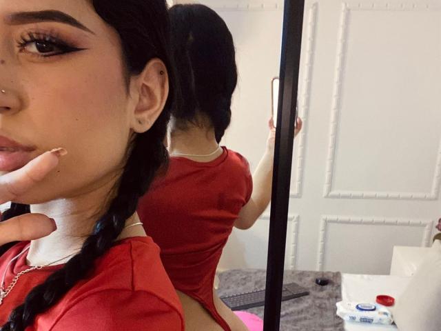 AnnaTorress with braided black hair, red shirt, showing her ass in mirror selfie. Her finger touches her cheek, and she has a nose ring. Her back is to the camera.