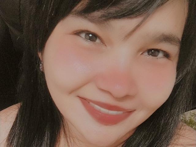 PrittyAlicia with black hair, brown eyes, and a pinkish blush on her cheeks, smiling with red lipstick, showing a cute, soft-faced, sexy ass-kissing look.