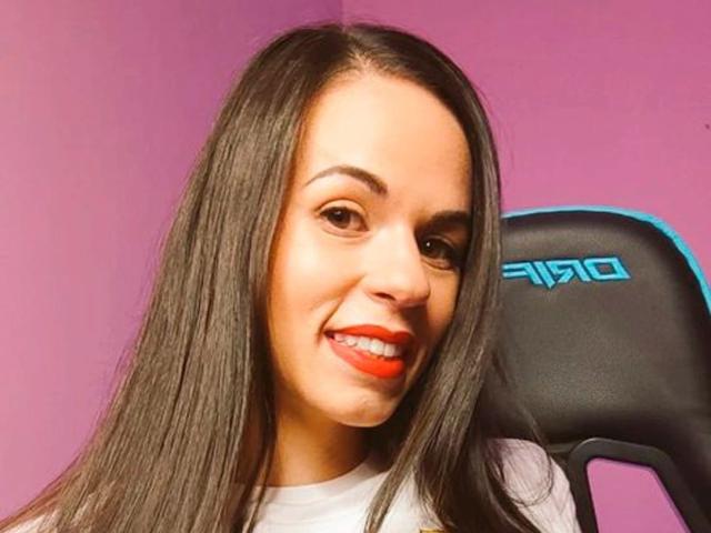 Nekane-hot with long straight black hair, brown eyes, red lipstick, smiling, wearing white shirt, sitting in black chair with blue accent.