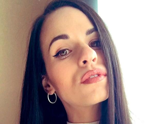 Nekane-hot ha i capelli castano scuro, sopracciglia folte, eyeliner, rossetto rosa, orecchini a cerchio e un leggero sorriso, guarda di lato con uno sfondo luminoso..