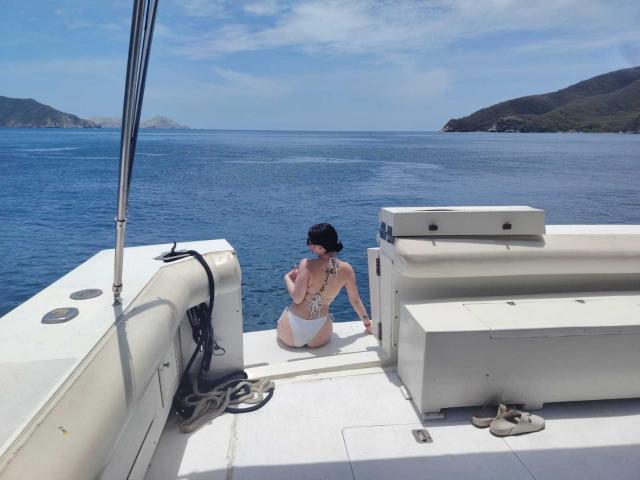 AnntonellaWatson, back to camera, white bikini, black cap, kneeling on boat, blue sea, white boat, black rope, tan sandals, white storage, clear sky, daytime, short hair.
