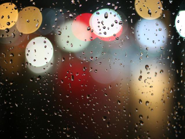 Water droplets on a window with blurred, colorful bokeh lights in the background. Boob-like water droplets cover the window, reflecting soft light. MissSunshine-hot's sexy city night view.