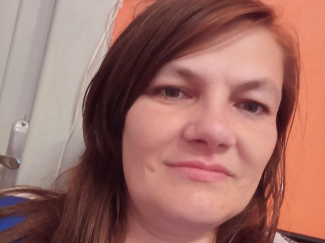 Kopretinka has light brown hair, a small mole under her right eye, and a slight smile with closed lips. Her skin is fair, and she has small tits.