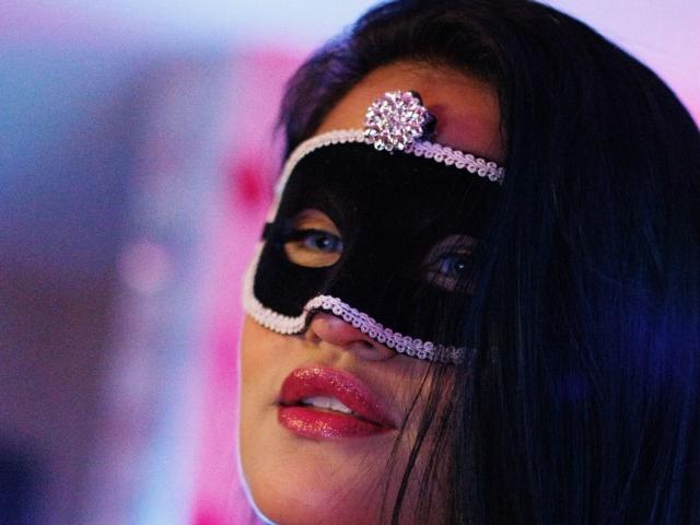 KiaraDaSorteOF has shiny red lips, a black mask with pink diamond trim, and a pink diamond headpiece, with long black hair covering the right side of her face.