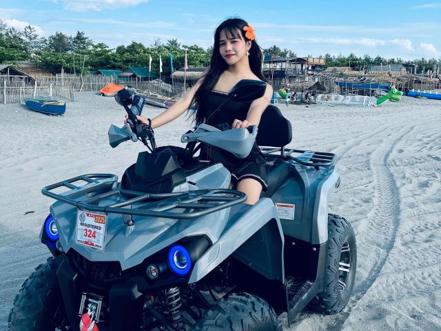 FRESHotBHEAx-hot with long black hair and orange hairclip, sitting on a gray ATV, wearing a black strapless top, smiling, holding the handlebars, on a sandy beach.