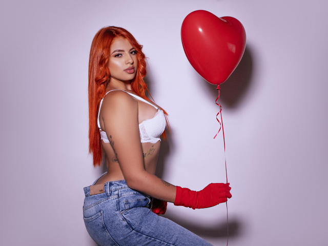 SherylRobhinss with red hair, white bra, blue jeans, red gloves, holding red heart balloon, tattoos on side, sexy, cute, looking over shoulder, white background.