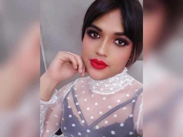 SweetNatashaX with short black hair, red lipstick, and dramatic eye makeup, wearing a sheer polka-dot dress with lace trim, touching her cheek. Her tits are visible through the dress.