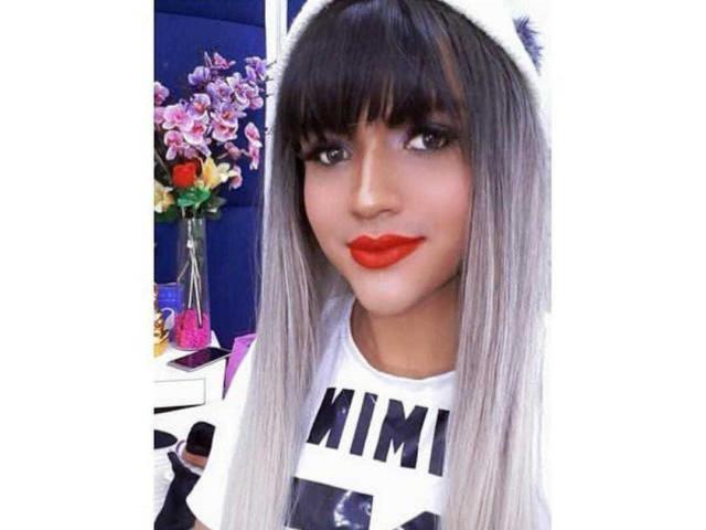 SweetNatashaX with long gray-brown hair, white hat, red lipstick, and white shirt, holding black object, looking cute and sexy. Boobs not visible, pussy not visible, ass not visible.