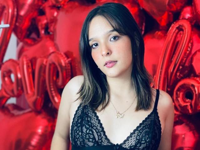 LanaKlyne with medium tits, wearing black lace lingerie, has light brown skin, straight brown hair, and a "W" necklace, in a red balloon-filled background. She looks cute and sexy.