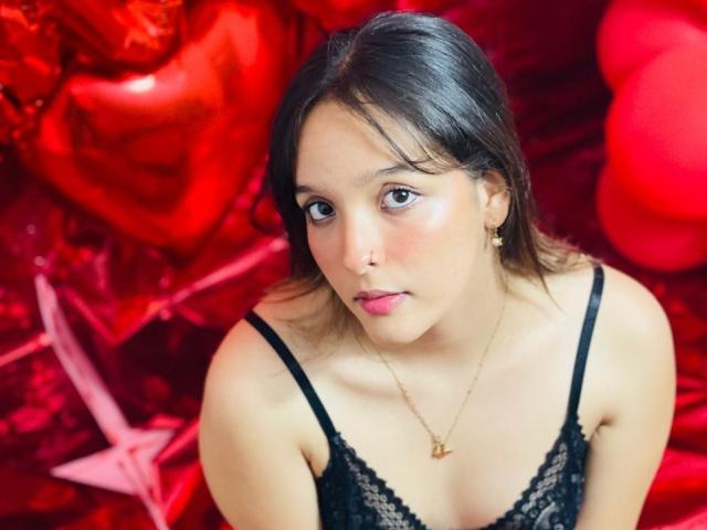 LanaKlyne with medium tits in black lace, looking up with a slightly pouty face, wearing a gold necklace, in a red, shiny, crinkled background.