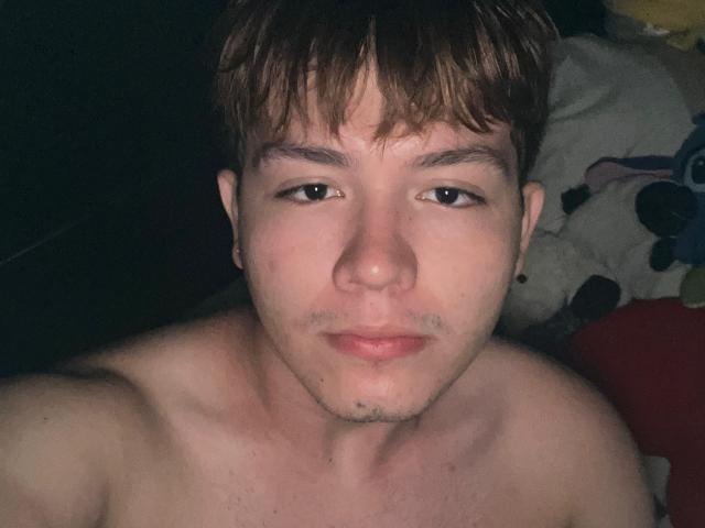 ErosDelRey, shirtless, with brown hair, slightly parted lips, and a neutral expression, staring into the camera, showing a clean-shaven face and subtle chest hair.