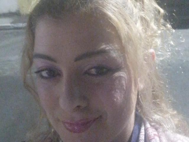 CrislimaJb has light blonde hair, purple eyeshadow, and is smiling with pink lipstick. Her face is slightly illuminated, showing a small bruise on her right cheek.