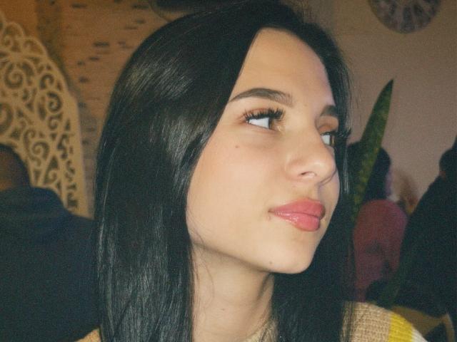 OliviaFoxy has black hair, light skin, and glossy pink lips, with long eyelashes and a slight pout, looking to the side. Her nose is small and cute.