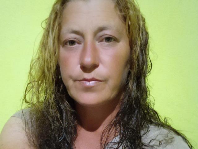ClaireApple has wet, shoulder-length brown and blonde hair, a slightly flushed face, and a subtle smile. She's wearing a gray shirt. Her tits are small and her ass is unseen.