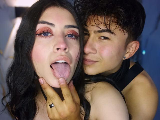 Noah y Rose, con sombra de ojos rosa, cabello negro y la lengua afuera, posando con la mejilla pegada. La mano de Rose muestra un anillo. Noah, con cabello negro, una camiseta negra sin mangas y detrás de Rose, sonriendo..