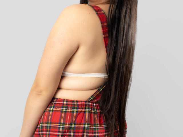 SaraFountain's back, wearing a red plaid skirt and a white bra, with long brown hair covering her right shoulder, exposing her bare back and sideboob.