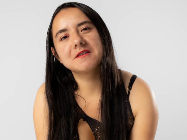 SaraFountain has long black hair, red lipstick, and is wearing a black mesh top, looking slightly up with a relaxed, slightly goofy expression. She has light skin.