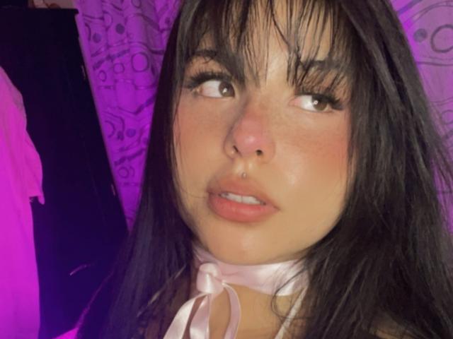 GraceClarke a les cheveux foncés, d'apparence mouillés, avec une frange, des yeux marrons et un piercing au nez. Elle porte un collier ruban blanc, ses lèvres roses légèrement entrouvertes. Elle lève les yeux avec un sourire discret..