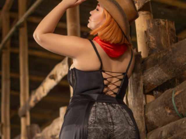 SummerJenna with orange hair, wearing a brown hat, black lace-up dress, and red scarf, has her back to the camera, showing her ass and lace-up design.