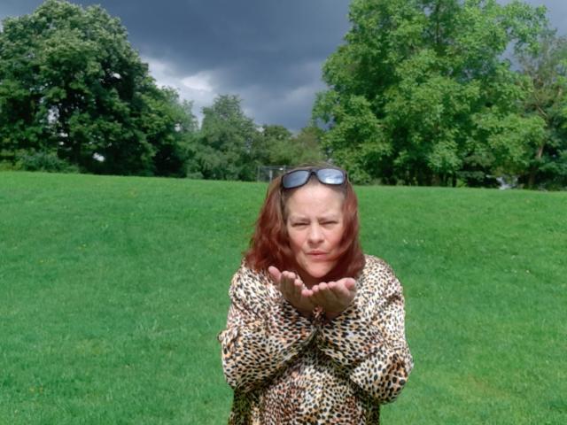 Kathy75-hot with red hair, leopard print jacket, and sunglasses on head, cupping hands under cloudy sky, green grass, and trees in background, looking slightly annoyed.
