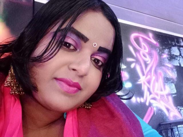 SusanaEshwarCurvy with pink eyeshadow, black hair, pink lipstick, red scarf, gold earrings, and a bindi, looking at the camera with a slight smile. Her tits are not visible.