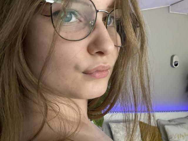 MagikPeachh tiene gafas, cabello castaño claro y una ligera sonrisa. Muestra su piel pálida y sus labios rosados, con una mirada sutil, relajada y sensual. Sus ojos son azules..