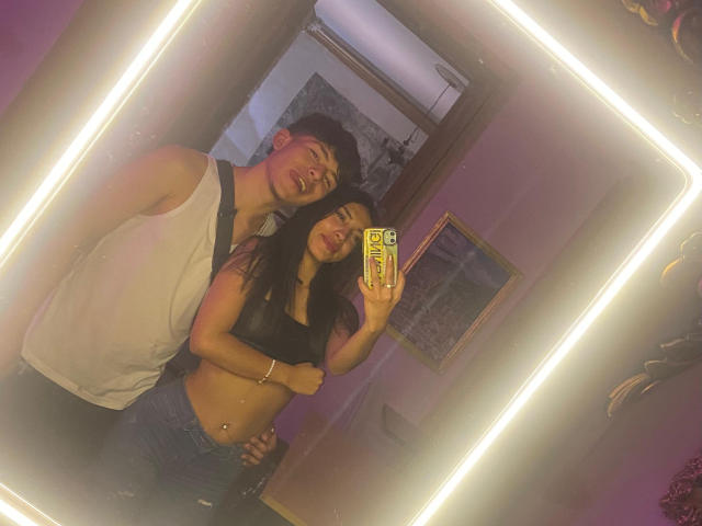 HotSweetLovers with dark hair, small tits, and a black crop top, stands next to HotSweetLovers with short hair, white tank top, and blue jeans in a mirror selfie.