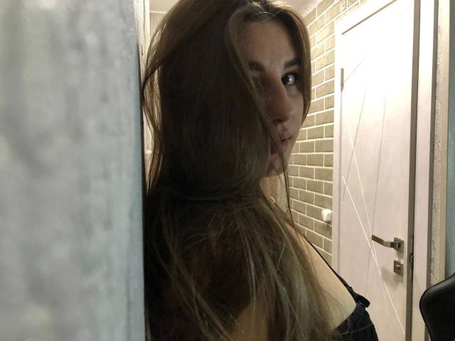 FlowerLeila-hot with long brown hair, looking over shoulder, black strap dress, subtle pout, soft light, brick wall, white door, slightly messy, sexy, seductive, partial profile.