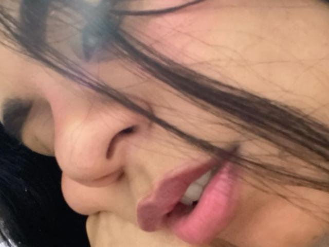MadissonWeel's face with dark hair covering her eye, her pink lips wrapped around a large, circumcised, erect penis. Her hand grips the base. Her skin is light.
