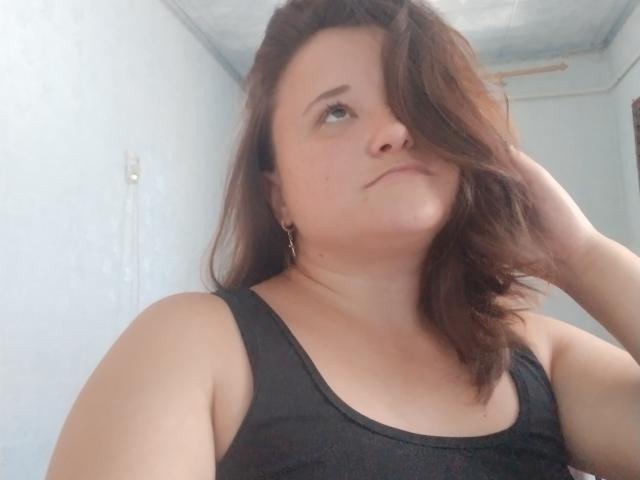 Annoying with brown hair, wearing a black tank top, has her head tilted, looking off to the side, with a slightly annoyed or indifferent expression.