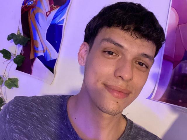 LinoRayn with short curly black hair, brown eyes, light skin, slight stubble, wearing a gray shirt, smiling subtly, purple-blue lighting, small leafy plant on the left.