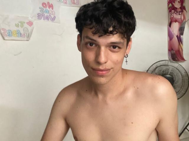 LinoRayn, shirtless, with short curly black hair, small cross earring, light skin, subtle smile, slight pimple on chin, small nipples, standing in front of a fan.