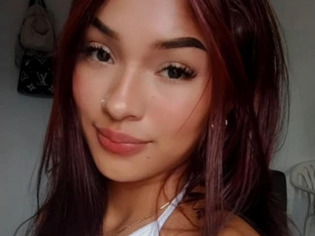 SashaHans has dark red hair, a cute nose ring, and full pink lips with a slight smile. She's looking at the camera with big, dark eyes.