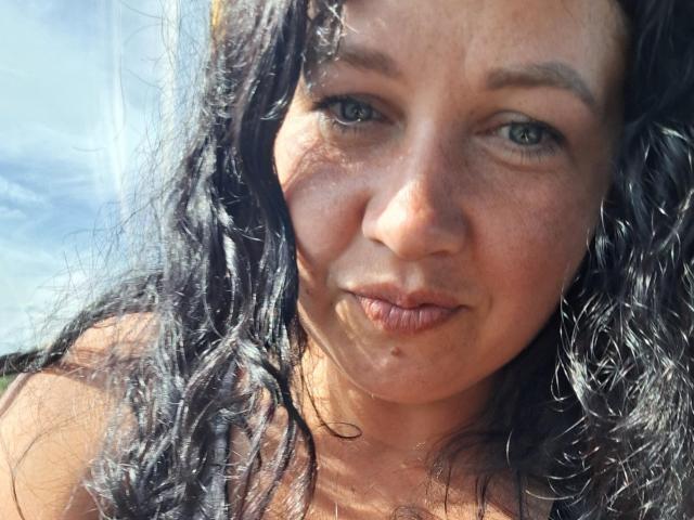 WestNancy's face with curly black hair, blue eyes, and slightly parted lips, showing a small drop of clear liquid on her chin. She's smiling softly, looking straight at camera.