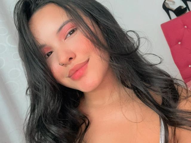 ArianaSmith69 has long black hair, pink eyeshadow, and a small nose ring, smiling with pink lips, wearing a white tank top, and looking cute with soft skin.