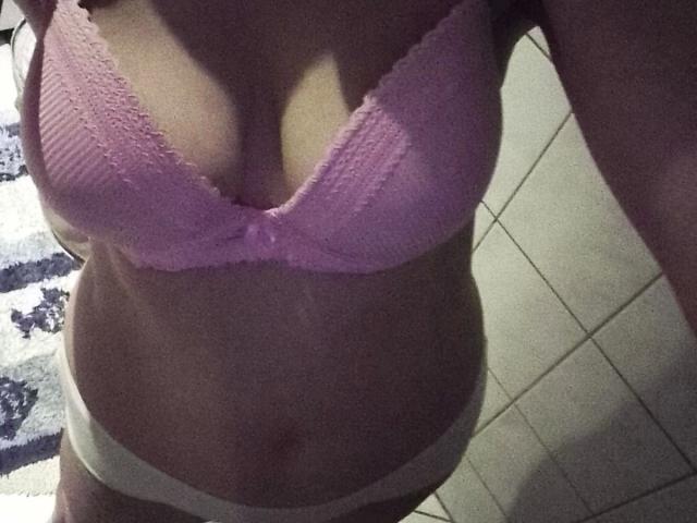 Sexybienchen93-hot in pink lace bra, showing medium-sized boobs, and white panties, with a slightly visible belly and tan lines, in a dimly lit room.