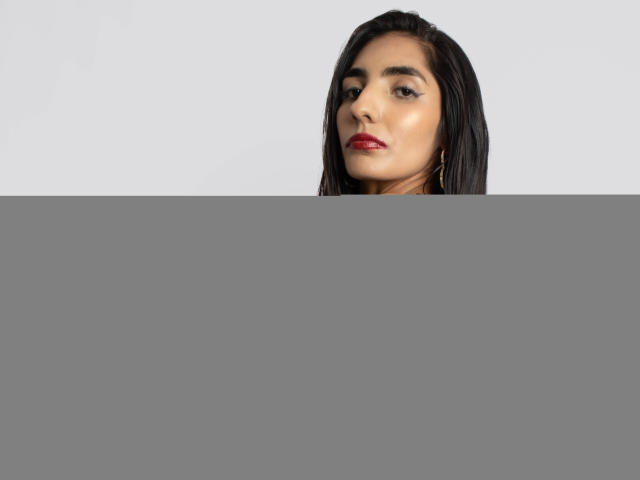 JuicyRoseX with long black hair, red lipstick, blue strapless dress, bare shoulders, looking over shoulder, light skin, subtle makeup, small gold hoop earrings, side profile, confident.