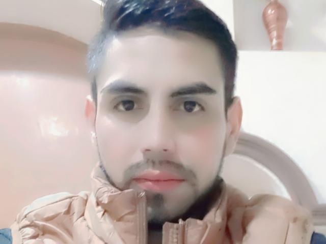 BisexualInteract has a light skin tone, short dark hair, and a beard, wearing a brown jacket, with a slightly blurry face and soft pink lips, looking straight at the camera.