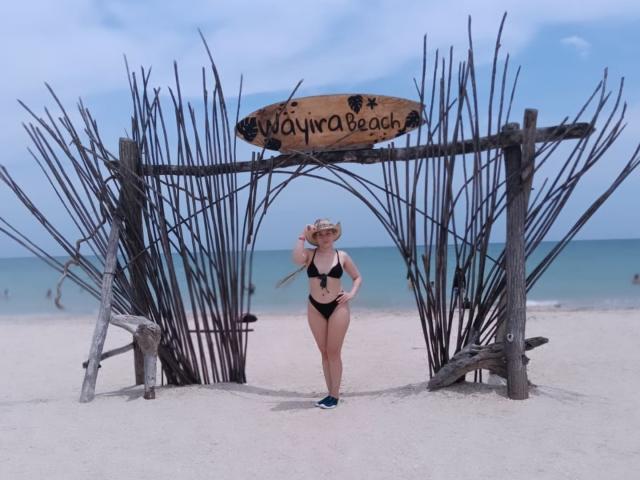 HaileyDavies stands in front of a wooden beach sign with a sign that says "Wayjina Beach," wearing a black bikini and a hat, with her tits and ass exposed.